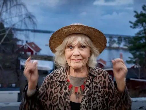 Christina Schollin, med sin karaktäristiska hatt och leopardmönstrade jacka, ser ut att berätta en historia från sina filmer och tv-program.