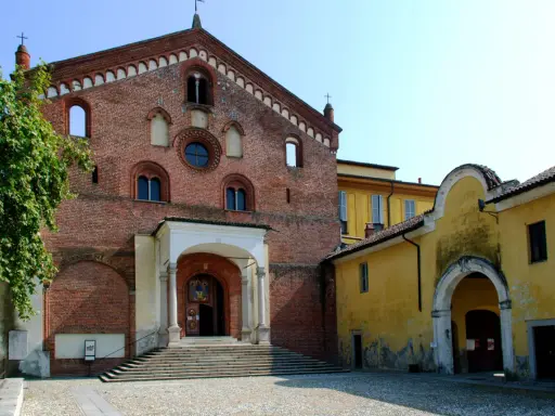 Morimondo cosa vedere: imponente facciata in mattoni rossi di un'antica abbazia, con scalinata e portico. Accanto, un edificio giallo con un arco.