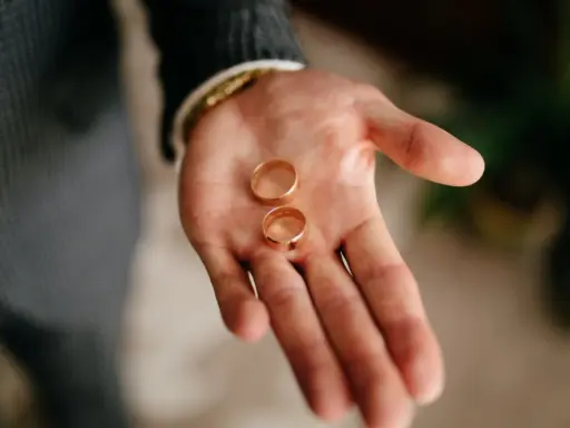 Dłoń mężczyzny trzyma dwie złote obrączki. To symbol miłości i tego, kto kupuje obrączki na ślub.