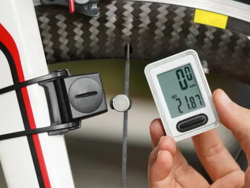 Rowerzysta sprawdza licznik pokazujący dystans 21.87 km. Obok widoczny czujnik na kole, który mierzy obwód koła rowerowego.