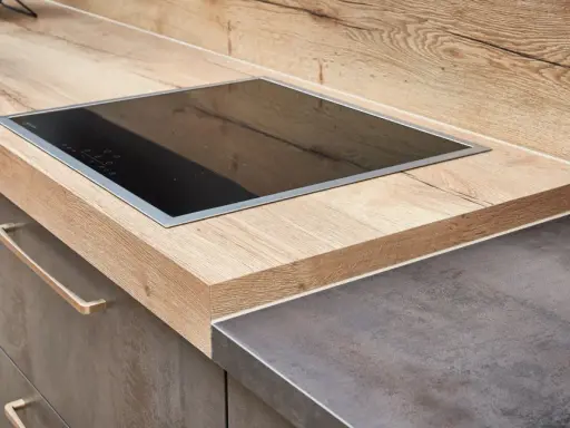 Eine moderne Küche mit einer Holzoptik-Arbeitsplatte und einem dunklen Stein-Arbeitsplatten-Material. Ein Kochfeld ist eingelassen.