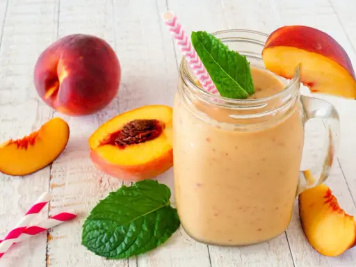 Erfrischender Pfirsich Smoothie im Glas, garniert mit Minze und Pfirsichspalten. Dazu frische Pfirsiche und Trinkhalme.