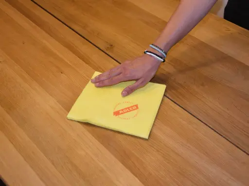 Hand wischt mit gelbem Tuch über Holzoberfläche, um den holztisch aufhellen.