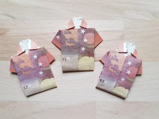 Drei Hemden aus gefalteten Euro-Scheinen. Kreative Geld Formen auf Holzhintergrund.