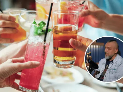 Ludzie wznoszą toasty kolorowymi drinkami. W tle mężczyzna dyskutuje, czy alkohol to narkotyk.
