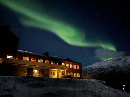 Norrsken över ett snötäckt landskap med ett hus. Perfekt för kiruna sightseeing turer.