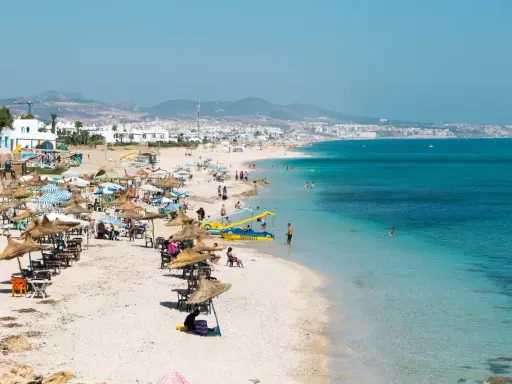 Spiaggia affollata in Marocco con bambini che giocano in acqua e famiglie che si rilassano sotto gli ombrelloni.