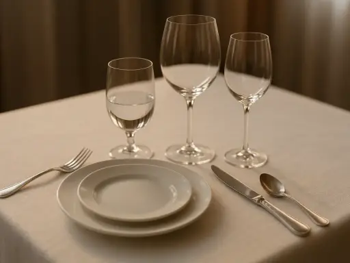 Un verre à eau, deux verres à vin vides, assiettes, couverts et une serviette sur une table dressée.