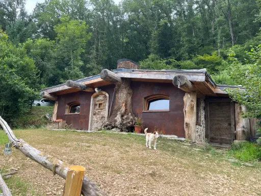 Une charmante cabane semi enterrée, intégrée à la nature, avec un chien curieux devant.