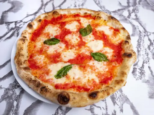 Pyszna pizza napoletana z pomidorami, mozzarellą i bazylią na białym talerzu, na tle marmurowego wzoru.
