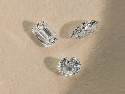Tre diamanti di taglio diverso (smeraldo, marquise, rotondo) su sfondo chiaro, pronti per la classificazione diamanti.