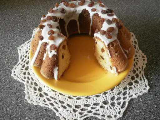 Pyszna babka drożdżowa z rodzynkami, polana lukrem i ozdobiona bakaliami, prezentuje się apetycznie na żółtym talerzu.