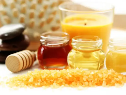 Ingredientes para un exfoliante corporal casero: sales, miel, aceites y una vela aromática.