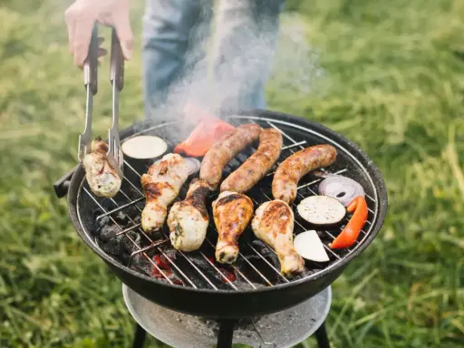 Rozpalanie grilla to sztuka! Na ruszcie skwierczą kiełbaski, kurczak i warzywa. Dym unosi się, zapowiadając pyszny posiłek.