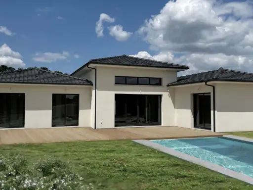 Une maison du sud moderne avec piscine, terrasse en bois et grand jardin sous un ciel bleu nuageux.