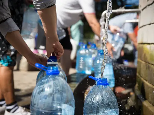 Menschen füllen Wasser in große Plastikflaschen. Die Frage, wie lange bleibt Wasser im Kanister frisch, ist hier relevant.
