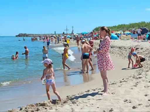Słoneczne wczasy pod gruszą na plaży. Ludzie kąpią się w morzu i opalają na piasku. Dzieci bawią się w wodzie i budują zamki z piasku.