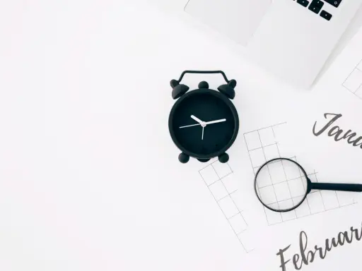 Czarny budzik, lupa i kalendarze z nazwami miesięcy. Zastanawiasz się, ile godzin ma etat?