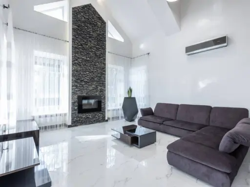 Sofá gris oscuro, chimenea de piedra, mesa de centro y suelo de mármol blanco.