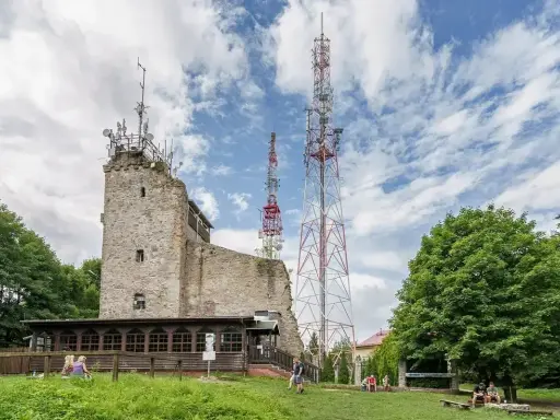 Kamienna wieża i wysokie maszty telekomunikacyjne na szczycie Chełmiec. Ludzie odpoczywają na trawie.