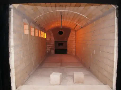 Wnętrze krematorium, gdzie czeka całun do kremacji. Pomieszczenie wyłożone cegłami, z łukowym sklepieniem i widocznym otworem pieca.
