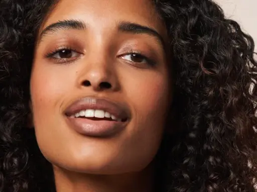 Ein Porträt einer Frau mit voluminösen, dunklen Locken, die die Curly Girl Methode perfektioniert. Ihre Haut strahlt, ihre Augen funkeln.