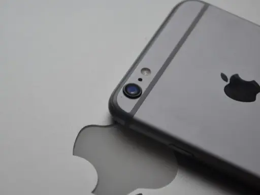 Srebrny iPhone leży na tle z wyciętym logo Apple, symbolizując spójność ekosystemu Apple.