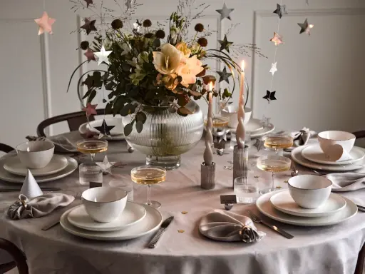 Vacker nyårsdukning med guldiga stjärnor, ljus och blommor. En elegant dukning för en festlig kväll.