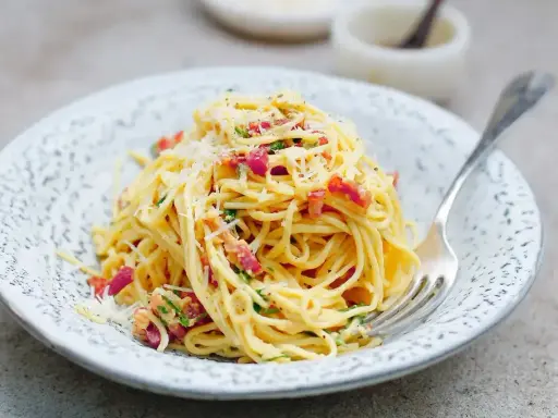 Pyszna carbonara ze śmietaną, okraszona boczkiem i parmezanem, czeka na widelcu.