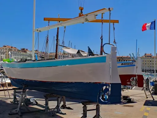 Un bateau hors de l'eau, prêt pour la maintenance, avec le nom "MARSEILLE" peint sur sa coque. Le drapeau français flotte au loin.