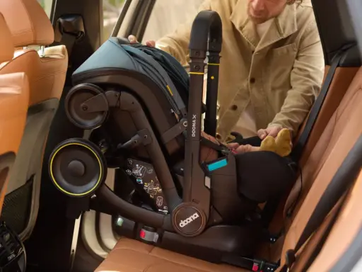 Mężczyzna wyjmuje fotelik z isofix z samochodu. Widać uchwyt i koła fotelika.