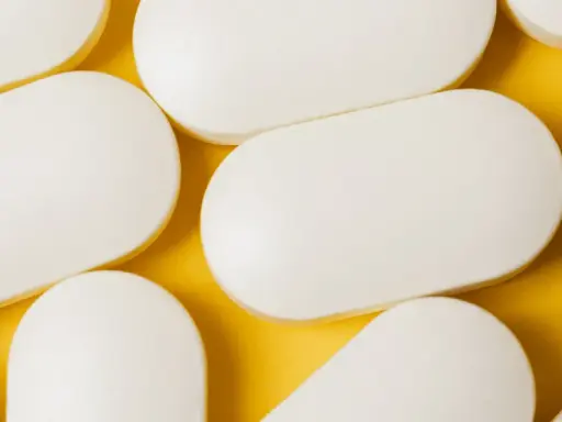 Bianche compresse ovali, disposte su sfondo giallo. Potrebbero essere un antibiotico azitromicina, utili per combattere infezioni batteriche.