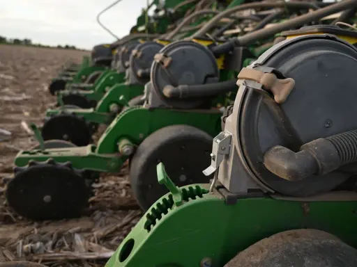 A row of green planters sits in a field, ready for planting. These machines are essential for farmers, contributing to the average hours on a tractor per year.