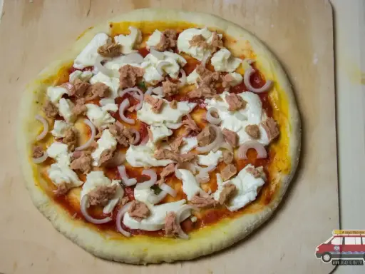 Gotowa do pieczenia pizza z tuńczykiem, mozzarellą i cebulą na drewnianej desce.