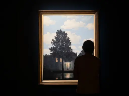 A person gazes at Magritte's "Empire of Light," a surreal scene of a house illuminated by a streetlamp under a daytime sky.