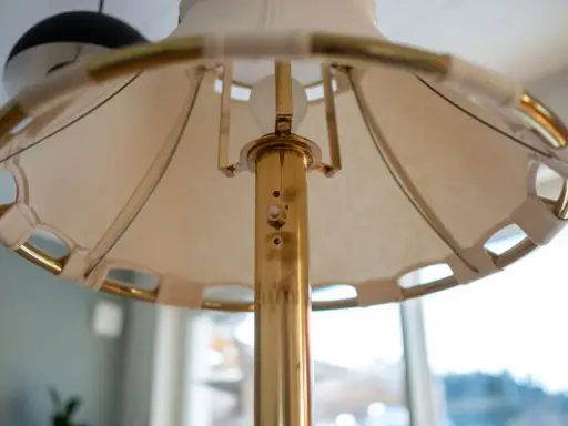 Detaljbild av en golvlampa i mässing från Ateljé Lyktan. Skärmen är av tyg med mässingsdetaljer.