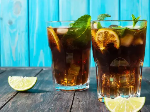 Dwa drinki z rumem, lodem, cytryną i miętą na drewnianym stole.
