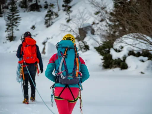 Dwóch alpinistów w zimowych strojach, z plecakami i sprzętem, przemierza ośnieżony teren. To inspiracja, co zabrać w góry zimą.