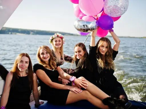 Uśmiechnięte kobiety na łodzi z balonami, celebrujące organizację wieczoru panieńskiego.