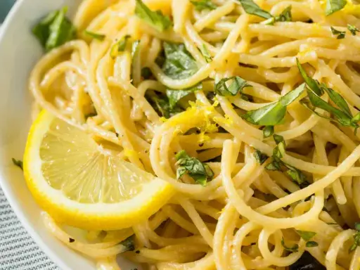 Spaghetti al limone cremosi, guarniti con scorza di limone e basilico fresco. Un piatto invitante e profumato.