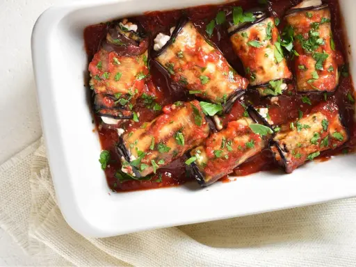 Involtini di melanzane ripieni di formaggio, cotti in sugo di pomodoro e guarniti con prezzemolo fresco.