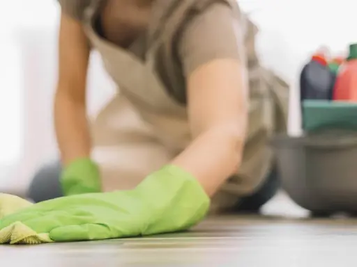 Rękawiczka w zielonym kolorze czyści linoleum. Obok miska z płynami do sprzątania, w tym ocet.