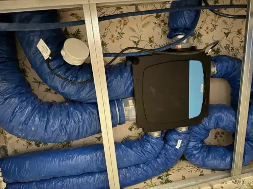 Système VMC installé dans un faux plafond. Les gaines bleues isolées sont connectées à une unité centrale noire. Un bon choix de VMC est essentiel pour la qualité de l'air intérieur.