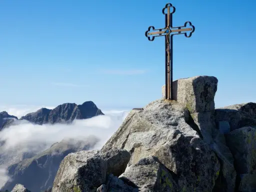 Krzyż na skalistym szczycie Gerlach. Widok na Tatry Wysokie ponad morzem chmur.