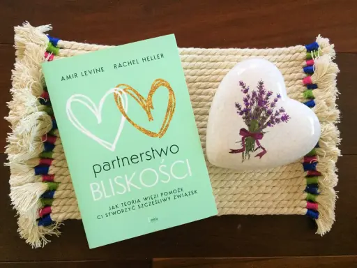 Książka "Partnerstwo bliskości. Jak teoria więzi pomoże Ci stworzyć szczęśliwy związek" obok serca z lawendą.