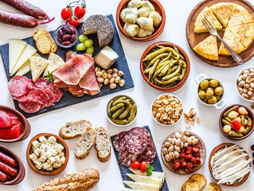 Una mesa llena de aperitivos baratos para mucha gente: embutidos, quesos, aceitunas, frutos secos, pimientos, pepinillos y pan.