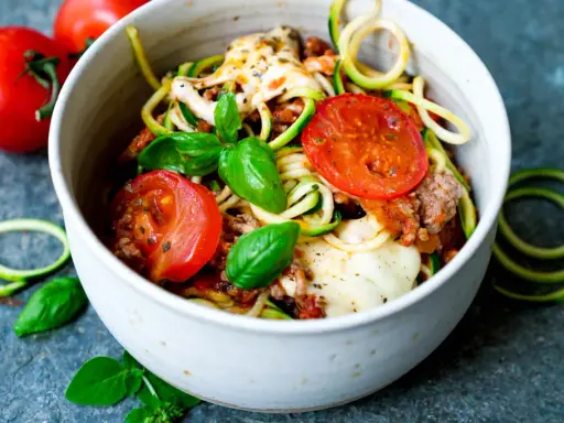 Herzhafte rezepte mit zucchini und hackfleisch: Zoodles mit Hackfleischsauce, Tomaten und geschmolzenem Käse, garniert mit frischem Basilikum.