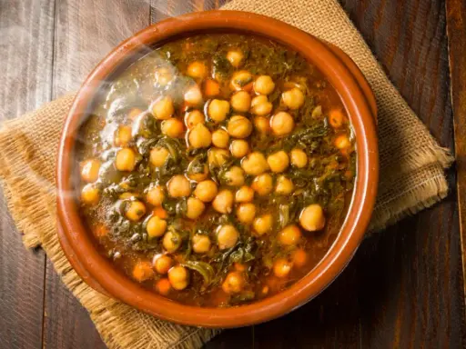 Cazuela de barro con garbanzos y espinacas, humeante y lista para servir. Se puede poner cazuela de barro en la vitro para cocinar este delicioso plato.
