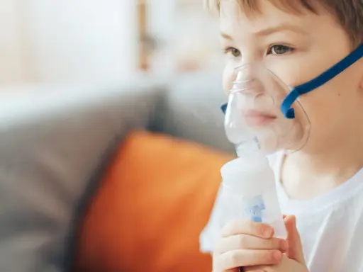 Chłopiec z maską inhalacyjną na twarzy, korzystający z nebulizatora. Pomaga mu to w leczeniu kataru.