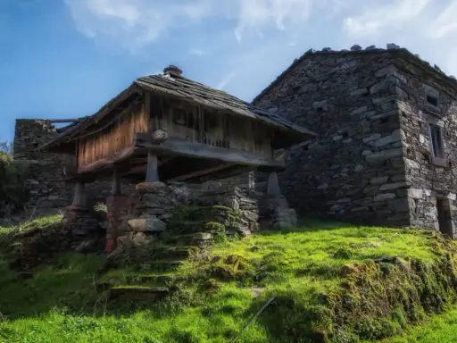Antiguos hórreos de piedra y madera, testigos de la ruta del silencio. Hierba verde y cielo azul.